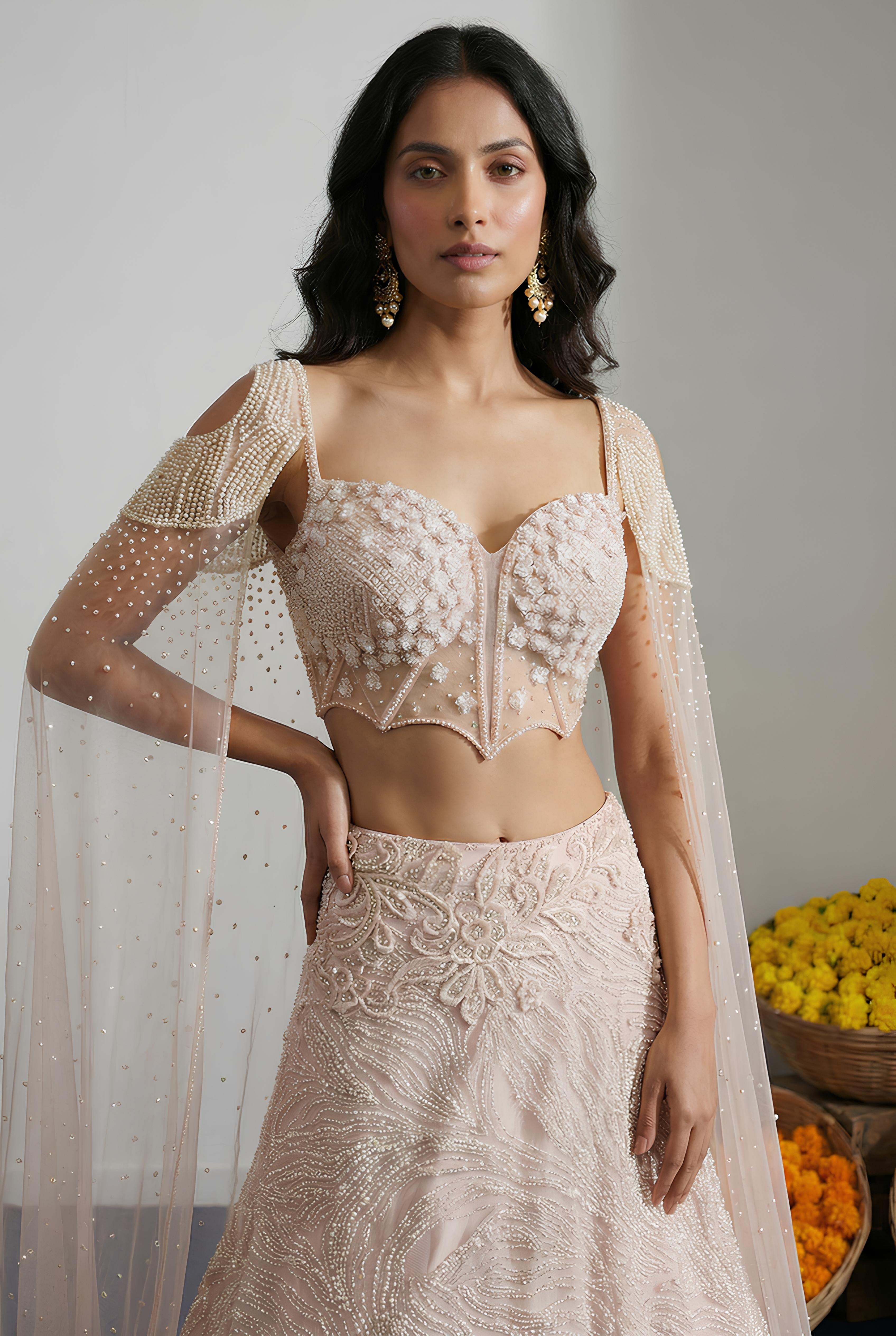 Woman wearing a traditional outfit with floral patterns and sheer sleeves against a neutral background.