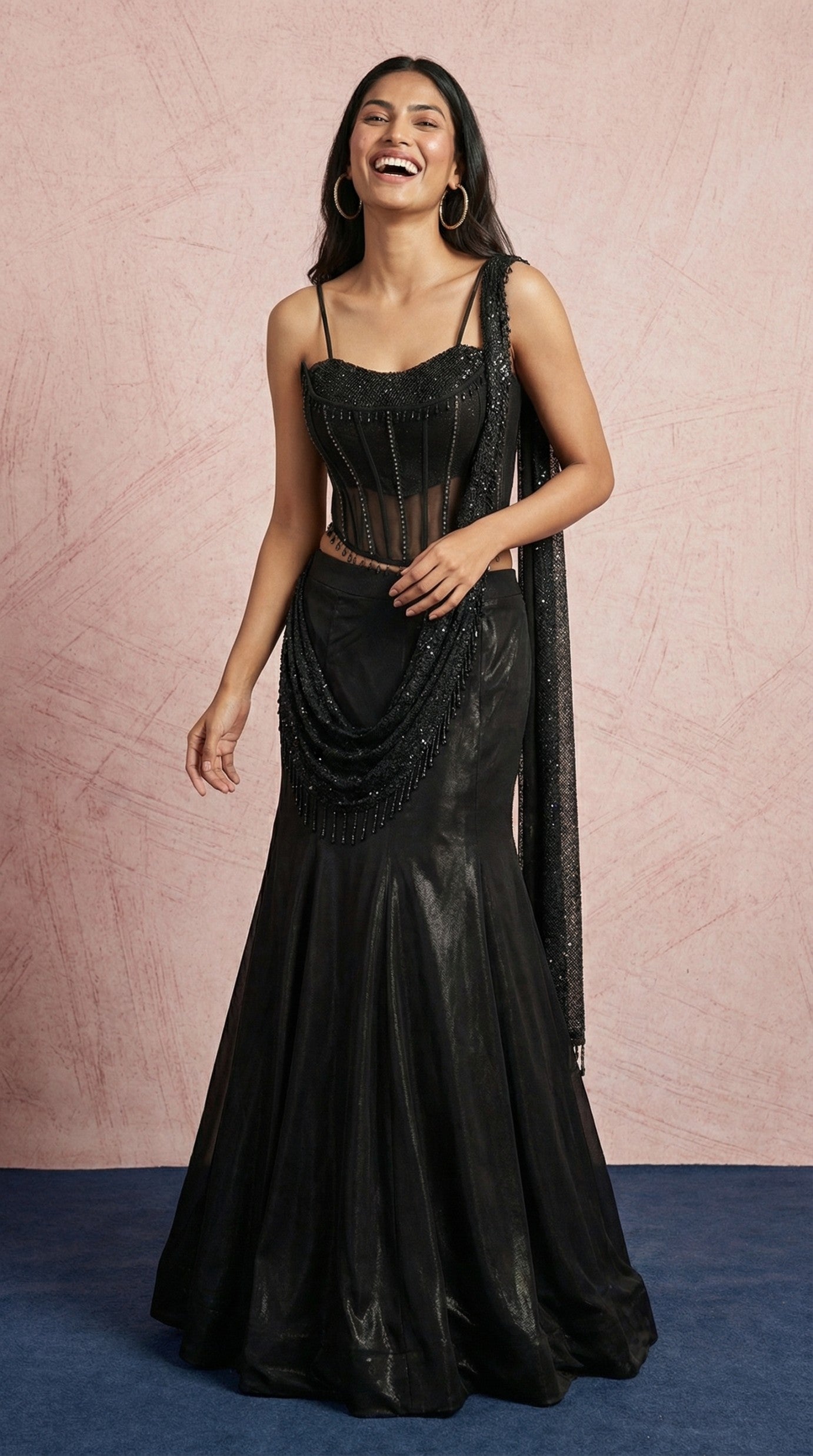 Woman wearing a black evening gown with a sheer overlay against a pink background